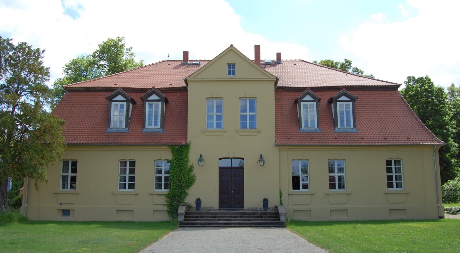 The manor house at Vollenschier: a rendered classicist building with a central pediment, mansard roof and eyebrow dormers