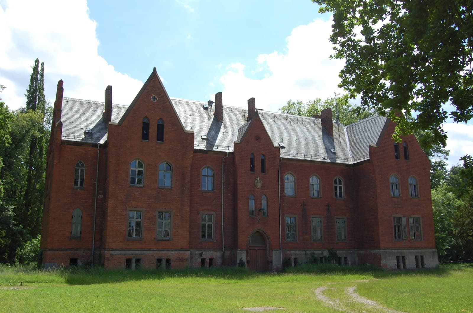 Vollenschier manor: two-storey neo-Gothic brick building with stepped gables, pointed-arch windows and an armorial stone above the portal